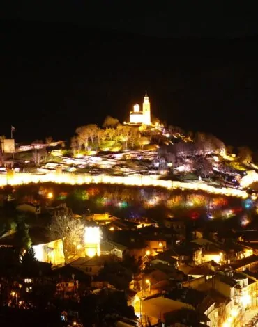 Vedere panoramică a spectacolului „Sunet și Lumină” Veliko Târnovo: cetatea Țareveț iluminată în noapte, vizibilă dintr-un punct de observație îndepărtat.