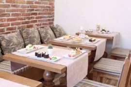 Десерти на маса - Уютно място с подредени десерти, сервирани на маса с дървени елементи и меки възглавници.