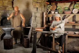 Figurine de ceară reprezentând doi bărbați, unul fierar lucrând la o nicovală, iar celălalt ceramică la o masă, înconjurați de opere de artă.