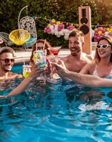 Група от шест души, млади и весели, поздравяват с тост в басейн на открито. Всички са облечени в бански и носат слънчеви очила. В ръцете си държат коктейлни чаши с различни цветни напитки. На заден фон могат да се видят удобни столове, колоритни балони и озвучителна система. Слънчевото време създава игриво и радостно настроение.